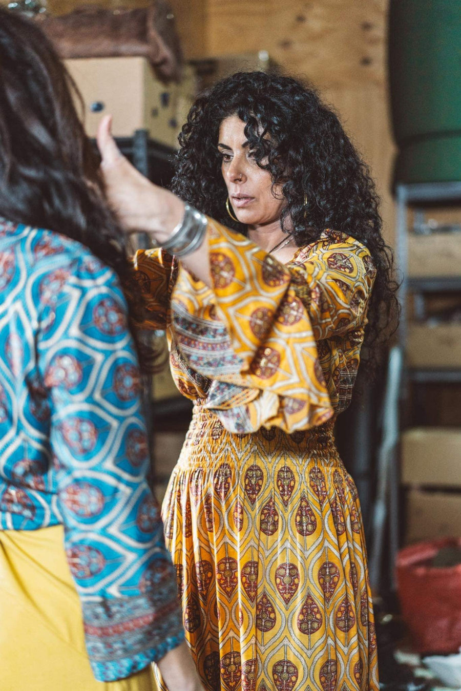 Woman in a patterned dress interacting with another person in a casual setting.